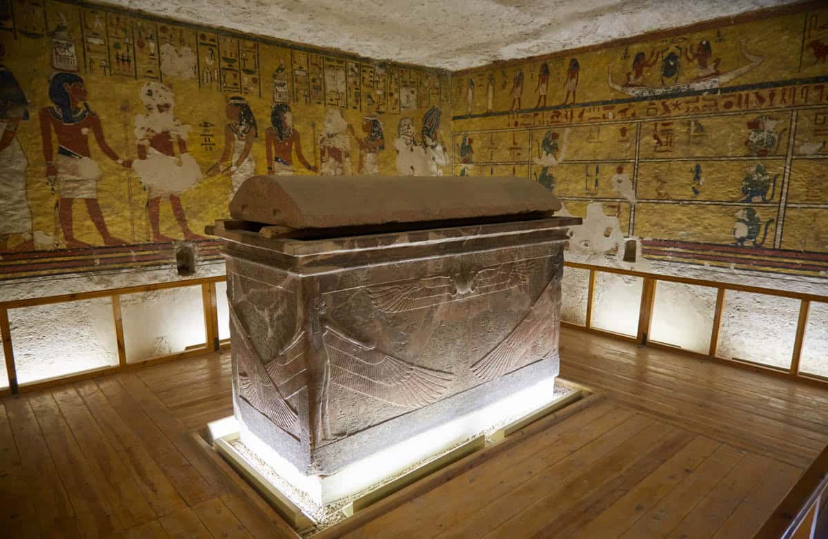 A dark stone sarcophagus stands within a painted chamber in the Valley of the Kings, Luxor, Egypt.