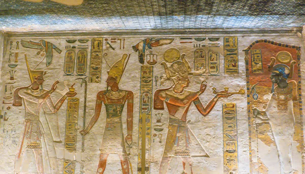 Painted standing deities and a royal figure on a hieroglyphic wall in the Valley of the Kings, Luxor, Egypt.