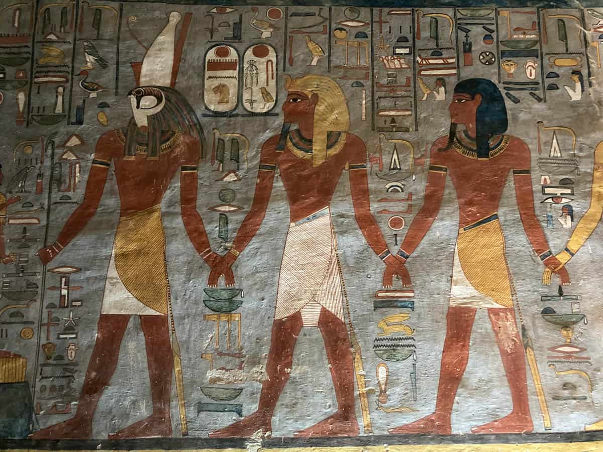 Colorful cartouches beside a royal figure and ancient deities in the Valley of the Kings, Luxor, Egypt.
